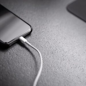 Smartphone connected to a charging cable on a dark textured surface.