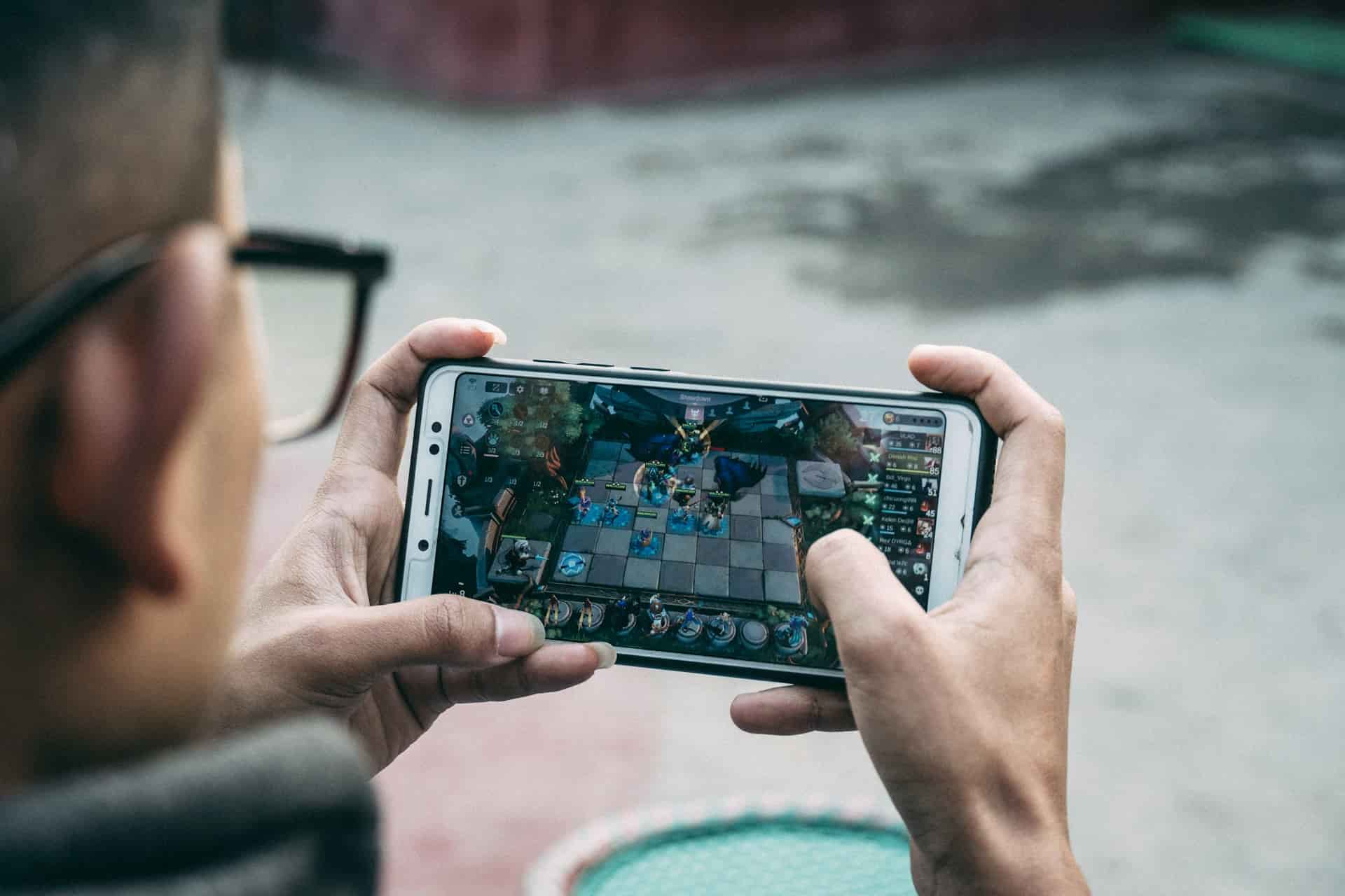 Close-up of a person holding a smartphone and playing a mobile strategy game with a chessboard-like interface.