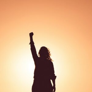 Silhouette of a person raising fist in the air against sunset, symbolizing power, strength and confidence – the 48 Laws of Powe